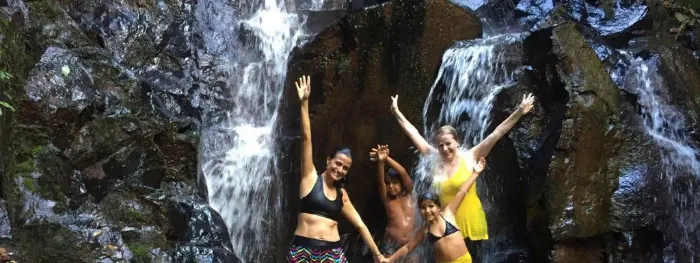Família se divertindo com os braços levantados tomando banho de cachoeira no viva brotas